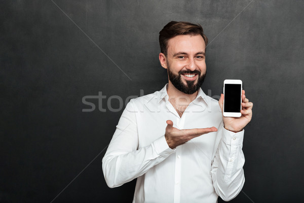 Positive brunette man showing smartphone on camera demonstrating Stock photo © deandrobot