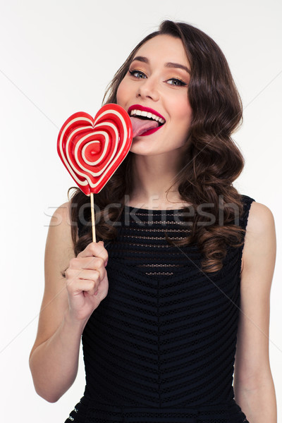 Content woman with retro hairstyle licking bright heart shaped lollipop Stock photo © deandrobot