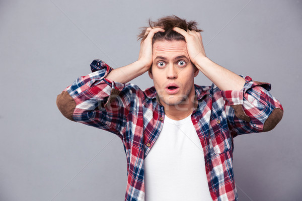 Shocked dazed young man holding head with both hands Stock photo © deandrobot