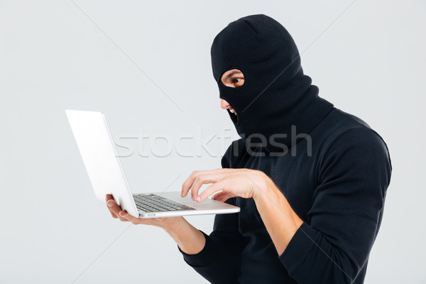 Portrait of man in balaclava standing and using laptop Stock photo © deandrobot