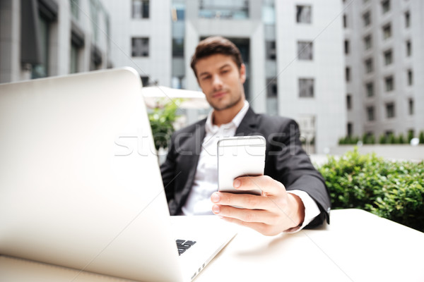 Businessman using laptop and cell phone in outdoor cafe Stock photo © deandrobot
