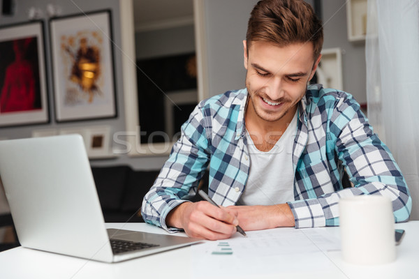 Cheerful bristle man using laptop computer while analyzing home finances. Stock photo © deandrobot
