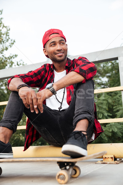 Happy dark skinned man sitting with his skateboard Stock photo © deandrobot