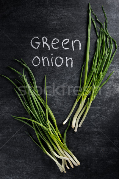 Photo of green onion over dark chalkboard background. Stock photo © deandrobot