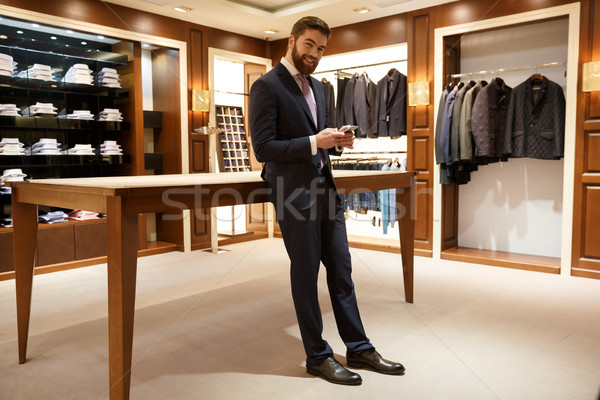 Full length portrait of happy man in suit holding  smartphone Stock photo © deandrobot