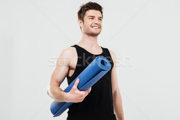 Smiling young sportsman holding fitness rug Stock photo © deandrobot