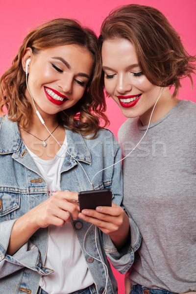 Cheerful women friends using mobile phone listening music. Stock photo © deandrobot