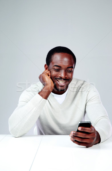 Stock photo: Cheerful african man sitting at the table and using smartphone
