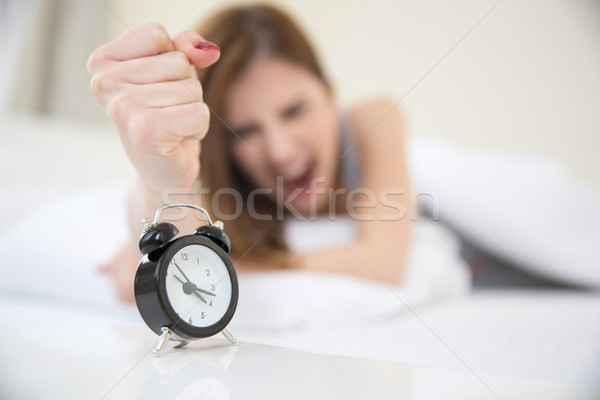 Young angry girl who woke up very early to call an alarm clock in the bedroom. Focus on clock Stock photo © deandrobot