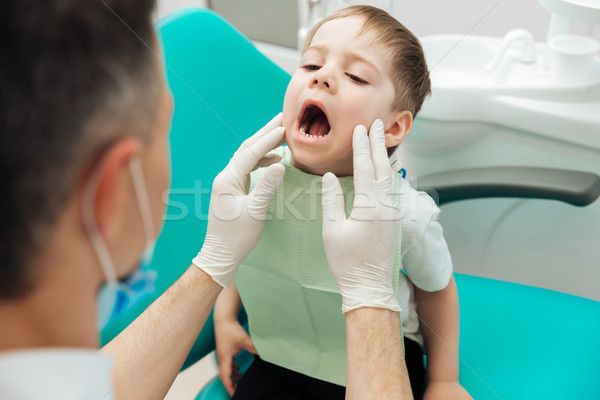 Dentist examining teeth of little boy witting with mouth opened Stock photo © deandrobot