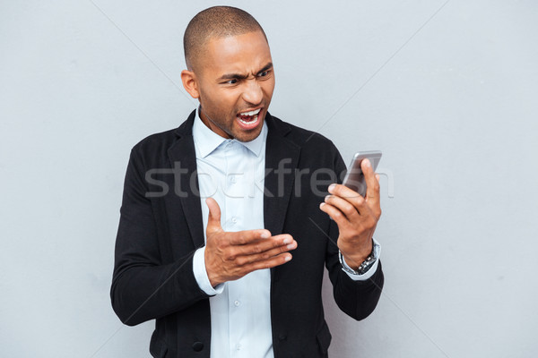 Man pointing with finger at smart phone isolated grey background Stock photo © deandrobot