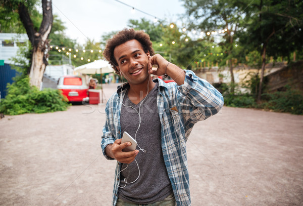 Stock photo: Smiling man in earphones listening to music from cell phone