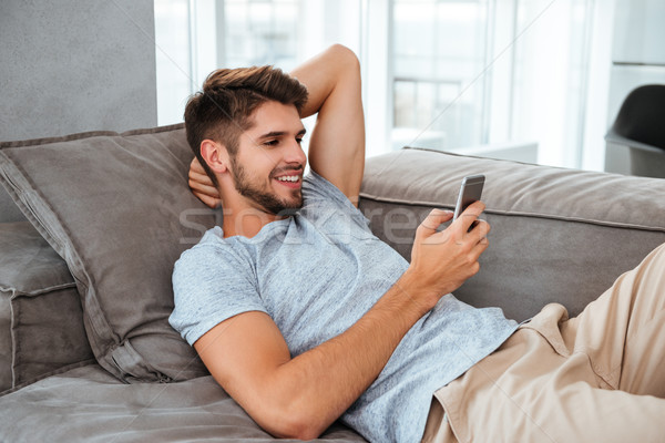 Happy young man lies on sofa and chatting by phone Stock photo © deandrobot