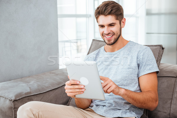 Happy man sitting on sofa and chatting by tablet Stock photo © deandrobot