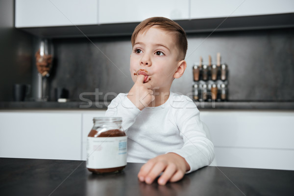 Cute boy standing in the kitchen while eating sweeties. Stock photo © deandrobot