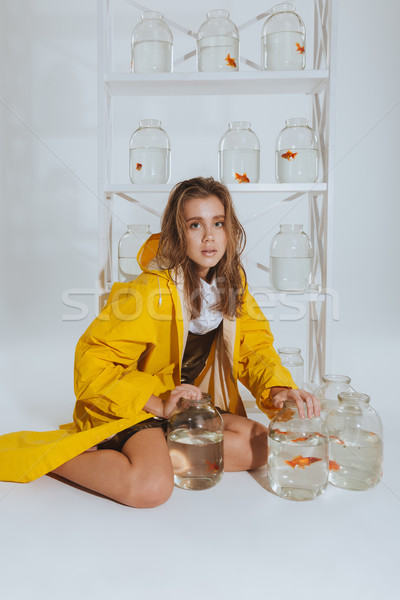 Woman in raincoat sitting and holding jars with gold fishes Stock photo © deandrobot