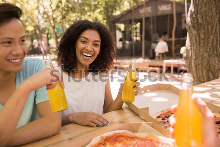 Smiling young multiethnic friends students outdoors drinking juice eating pizza. Stock photo © deandrobot
