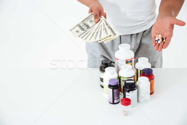 Cropped image of young sportsman holding vitamins and money. Stock photo © deandrobot