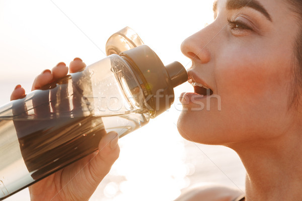 Close up of a pretty young sportswoman drinking water Stock photo © deandrobot