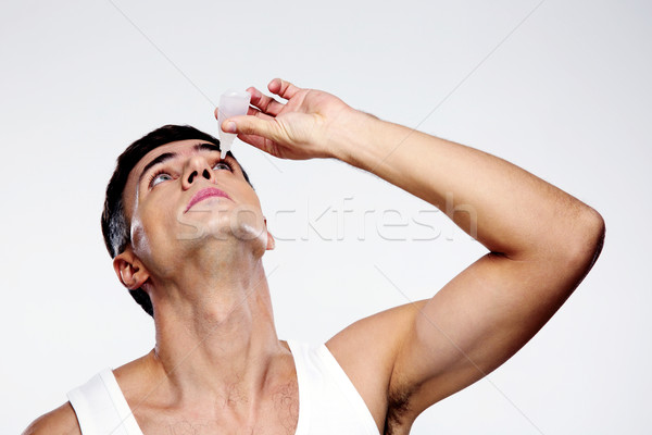 Handsome man applying eye drop over gray background Stock photo © deandrobot