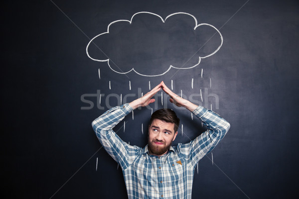 Frowning man covering from rain drawn on blackboard background Stock photo © deandrobot