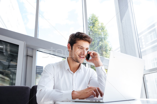 Happy young businessman talking on cell phone and using laptop Stock photo © deandrobot