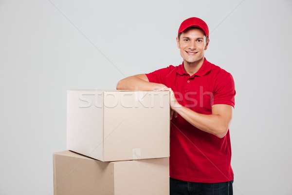 Happy smiling delivery man in red cap standing near boxes Stock photo © deandrobot