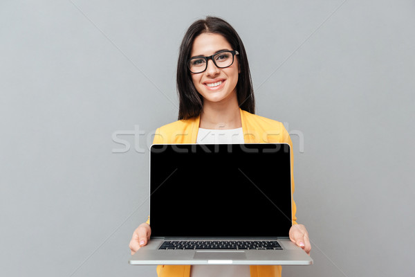 Stock photo: Pretty woman showing laptop display to camera over grey background