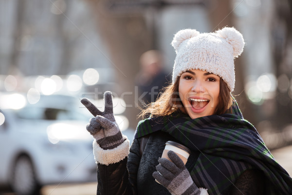 Cheerful woman drinking coffee and showing peace sign outdoors Stock photo © deandrobot