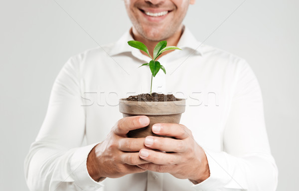Cropped image of young smiling man holding plant. Stock photo © deandrobot