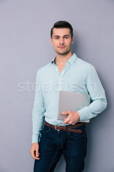 Homem bonito em pé laptop cinza olhando Foto stock © deandrobot