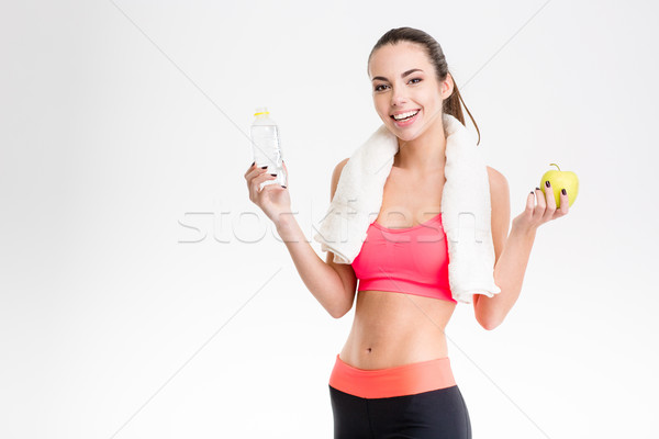 Cheerful sportswoman holding a bottle of water and an apple Stock photo © deandrobot