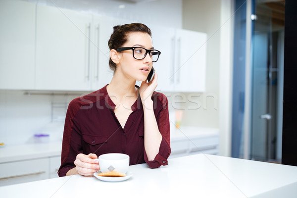 Woman in glasses drinking tea and using smartphone on kitchen Stock photo © deandrobot