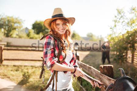 Cheerful smiling cowgirl preparing horse saddle for a ride Stock photo © deandrobot