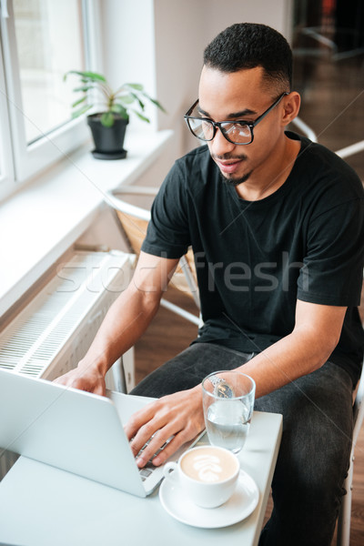 Attractive african businessman typing by laptop computer. Coworking. Stock photo © deandrobot