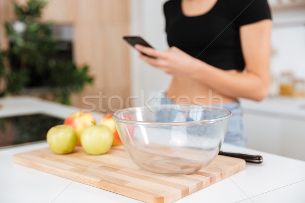 Cropped image of woman in kitchen using phone Stock photo © deandrobot