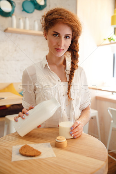 Pretty red haired woman pouring milk in glass from bottle Stock photo © deandrobot