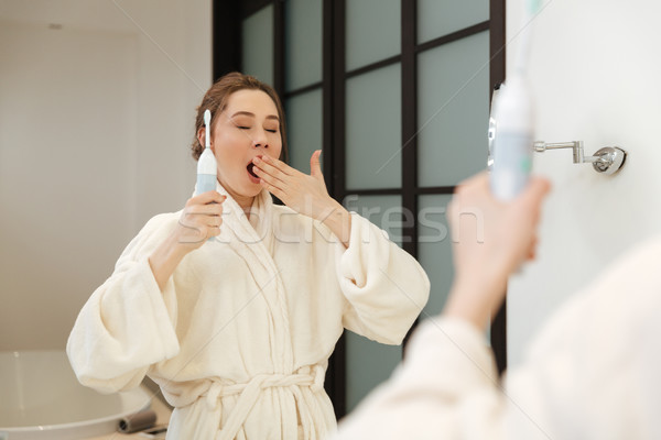 Stock photo: Sleepy relaxed woman yawning and brushing her teeth in bathroom
