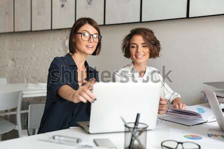 Two young laughing women working by the table Stock photo © deandrobot