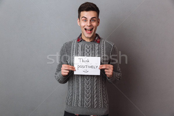 Happy screaming brunette man in sweater holding nameplate think positively Stock photo © deandrobot