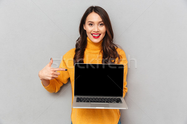 Happy brunette woman in sweater showing blank laptop computer screen Stock photo © deandrobot