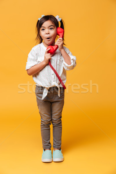 Shocked excited little girl talking by red retro telephone. Stock photo © deandrobot