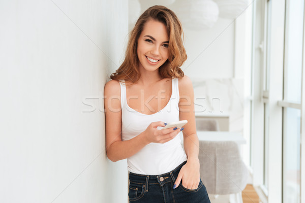 Happy young woman standing near window chatting Stock photo © deandrobot