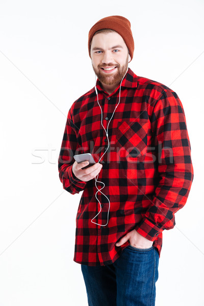 Smiling bearded man listening music with earphones over white background Stock photo © deandrobot