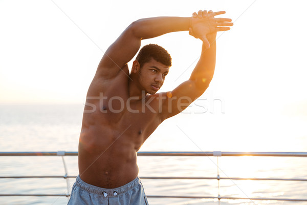 Handsome muscular african man athlete doing stretching exercises on pier Stock photo © deandrobot