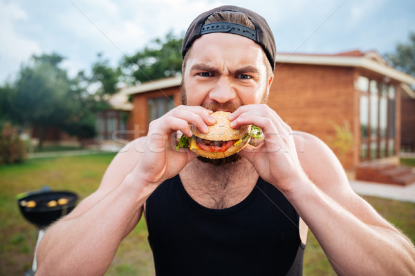 Young hipster guy eating delicious burger outdoors Stock photo © deandrobot