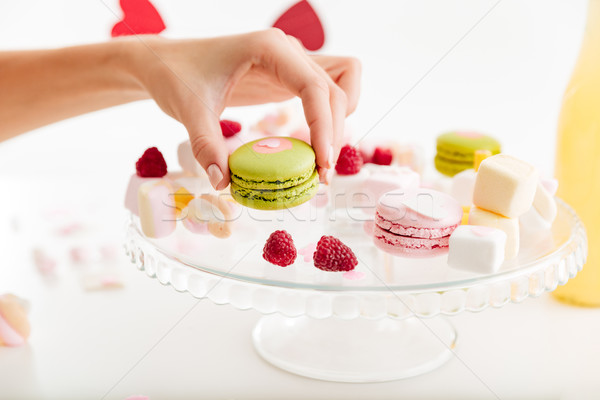 Hand taking green french macaroon from the plate with sweets Stock photo © deandrobot