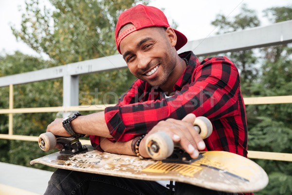 Cheerful dark skinned man holding skateboard Stock photo © deandrobot