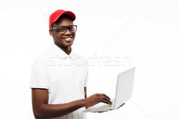 Stock photo: Happy young african man wearing cap using laptop computer