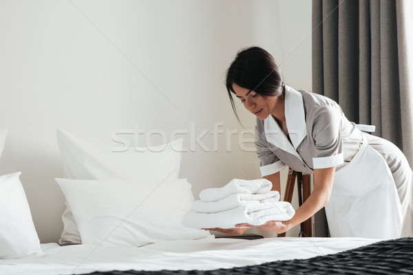 Young hotel maid putting stack of fresh white bath towels Stock photo © deandrobot